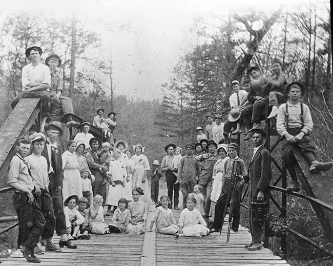 Group of white men women and children standing and sitting on steel bridge rails and platform