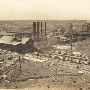 Aerial view of industrial buildings with smoke stacks and stacks of lumber in the foreground