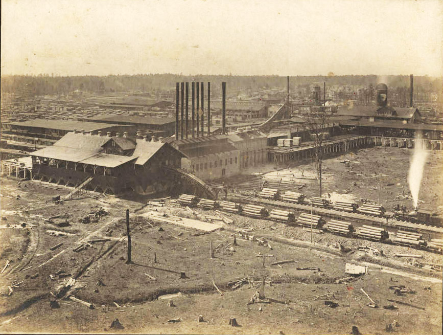 Aerial view of industrial buildings with smoke stacks and stacks of lumber in the foreground