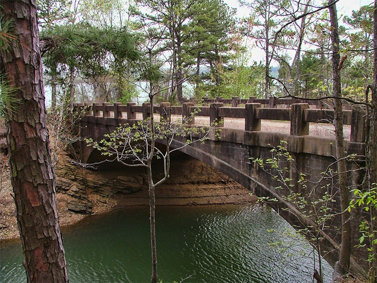 Concrete bridge over water with trees in background and foreground