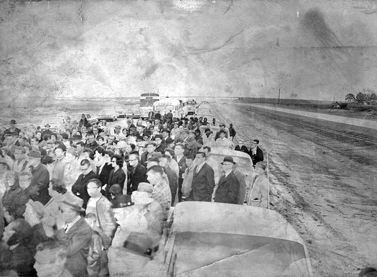 Crowd of white people standing with cars and buses on interstate