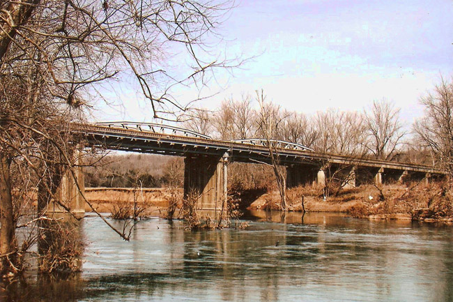 Concrete bridge over a river with trees and blue skies