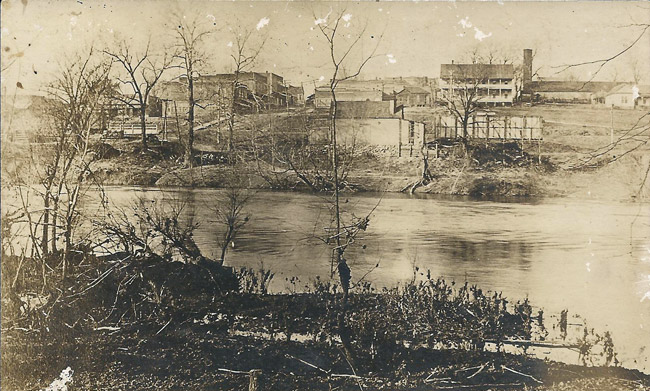 old faded photo of river with trees in the foreground and town in the background