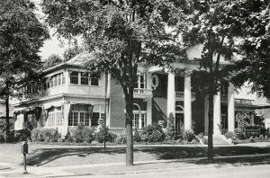 Multistory house with covered porch supported by four columns and trees on street
