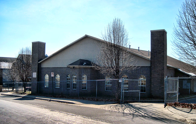 Single-story brick building with chain-link fence next to road