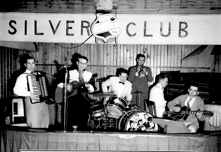 White musicians playing on stage under "Silver Club" banner