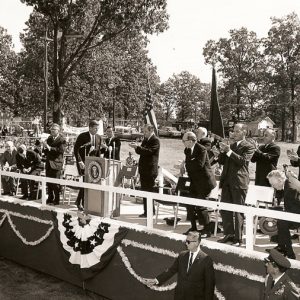 Decorated outdoor stage with white men and women clapping as a white man in suit approaches the lectern