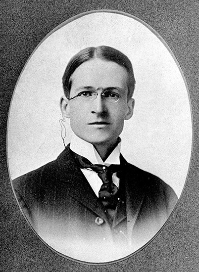 photo of young white man with glasses in suit and tie in oval frame