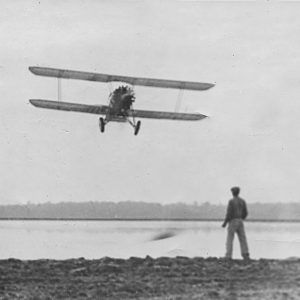 Man watching biplane flying over water