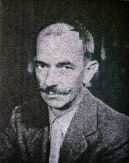 White man with curled up mustache in suit and tie