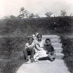 Three African-American children sitting on steps with houses in the far background