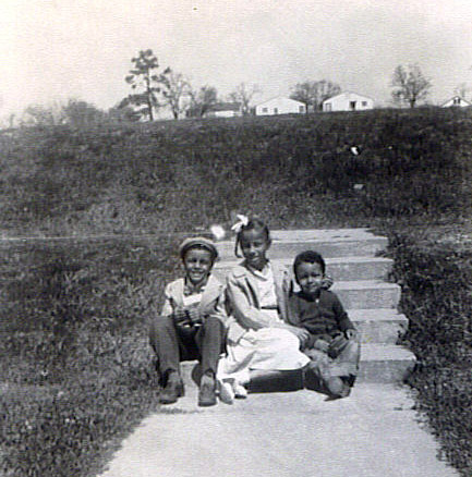Three African-American children sitting on steps with houses in the far background