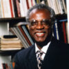 Portrait black man in suit and tie with glasses smiling in front of book case