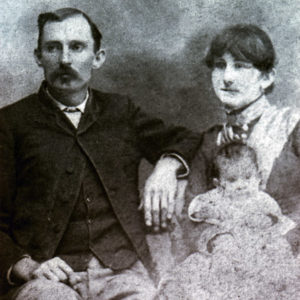 White man in suit with white woman in a dress holding a child sitting beside him