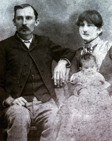 White man in suit with white woman in a dress holding a child sitting beside him