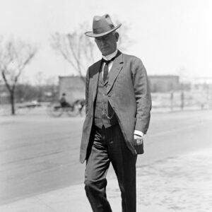 White man in suit wearing a hat with wagon and buildings behind him