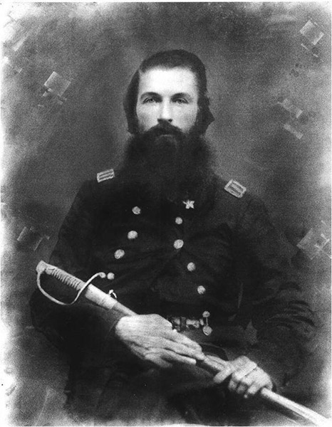 White man with long beard sitting in military uniform holding a sword across his lap