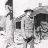 Young white man in military uniform standing with brick building and tree behind him