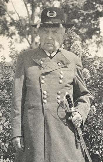 Older white man in hat and gray military uniform holding a sword