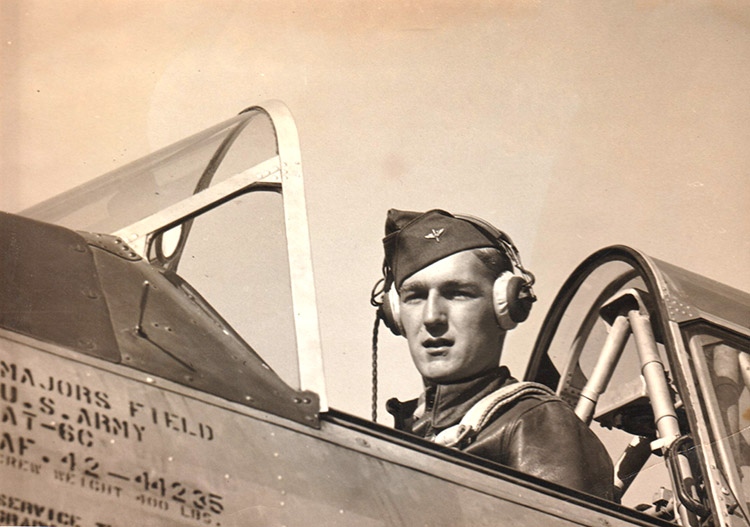 White pilot in open cockpit wearing military uniform with cap and headphones