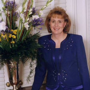 White woman in purple pantsuit with flowers in vase on table