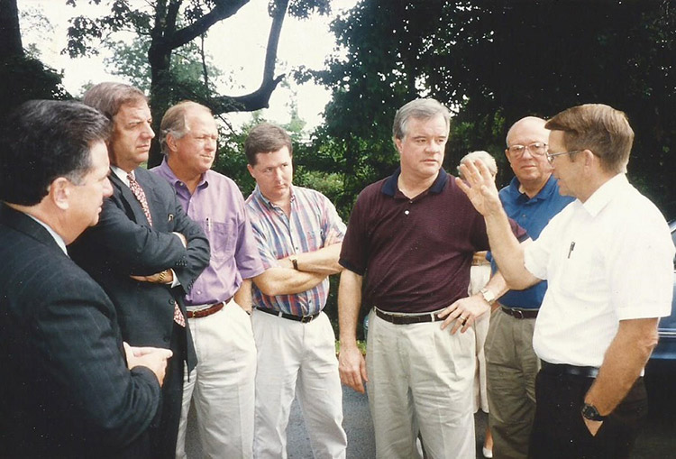 Group of white men standing together outdoors while one of them is speaking