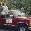 White man waving from bed of pickup truck with "Senator Jay Bradford" sign on its door