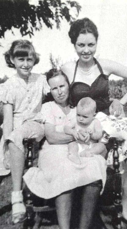 White woman standing behind older white woman and children sitting in a chair
