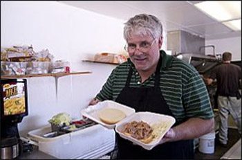 White man in striped shirt and apron serving food in restaurant