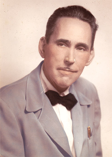 White man with pencil mustache and combed-back hair in pale suit jacket and black bow tie