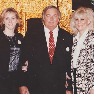 Two white women either side of one white man in suit and tie