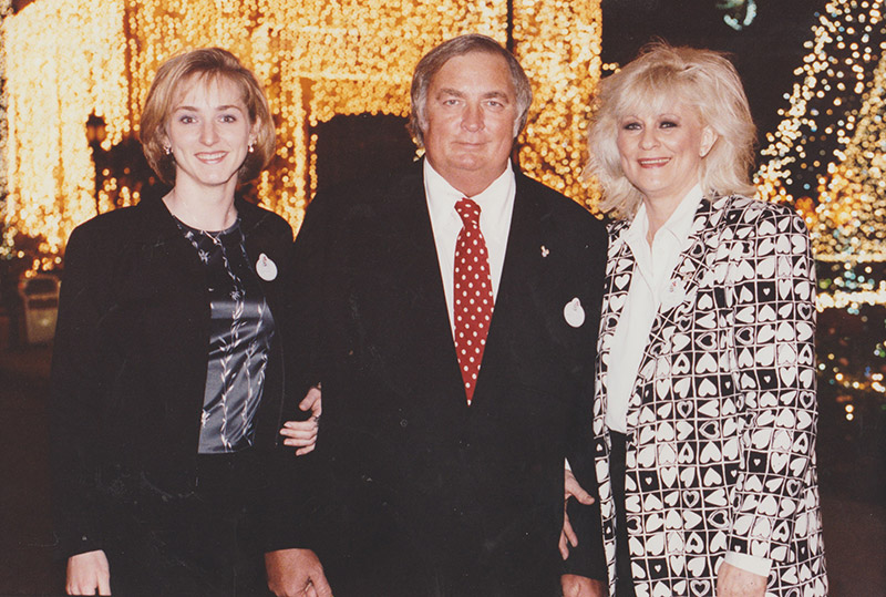 Two white women either side of one white man in suit and tie
