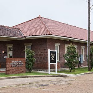 Single-story brick depot building with covered entrance and signs on parking lot