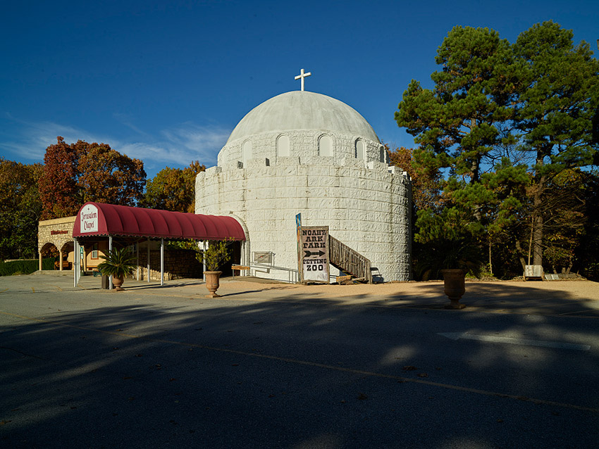 Round concrete building with dome and covered entrance on parking lot
