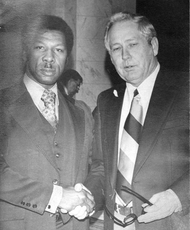 African-American man with mustache in suit standing next to older white man in suit and tie