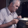 Older white man sharpening a knife blade at his desk