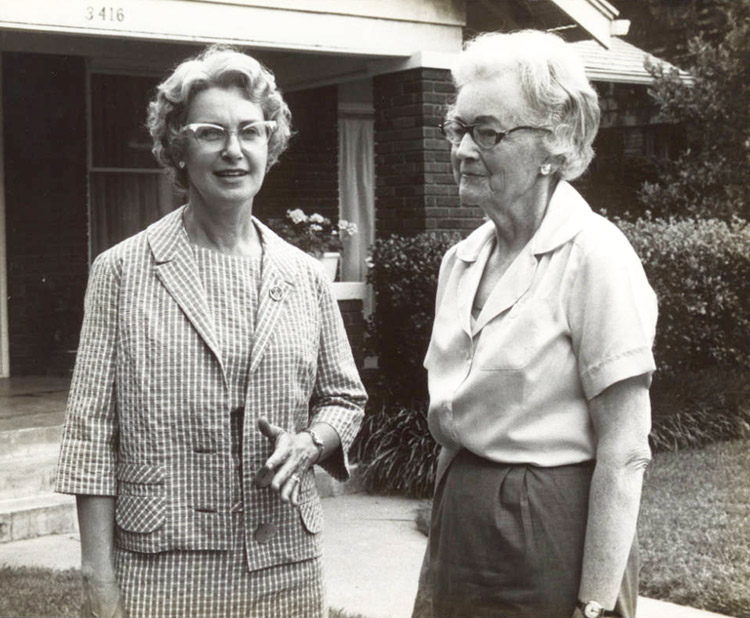 Pair of older white women with glasses standing outside house with covered porch