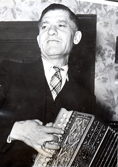 White man in suit and tie playing an accordion