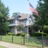 Multistory house with covered porch and flag pole inside iron fence on street corner