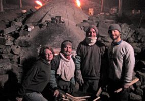 Three white men and one white woman with wheelbarrow filled with kindling and kiln behind them