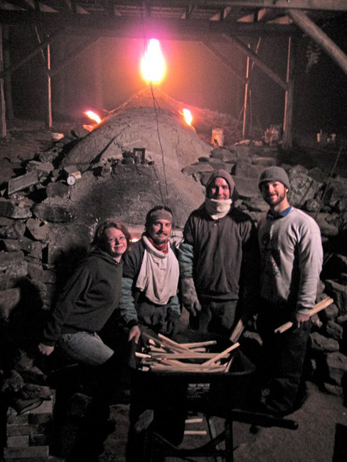 Three white men and one white woman with wheelbarrow filled with kindling and kiln behind them