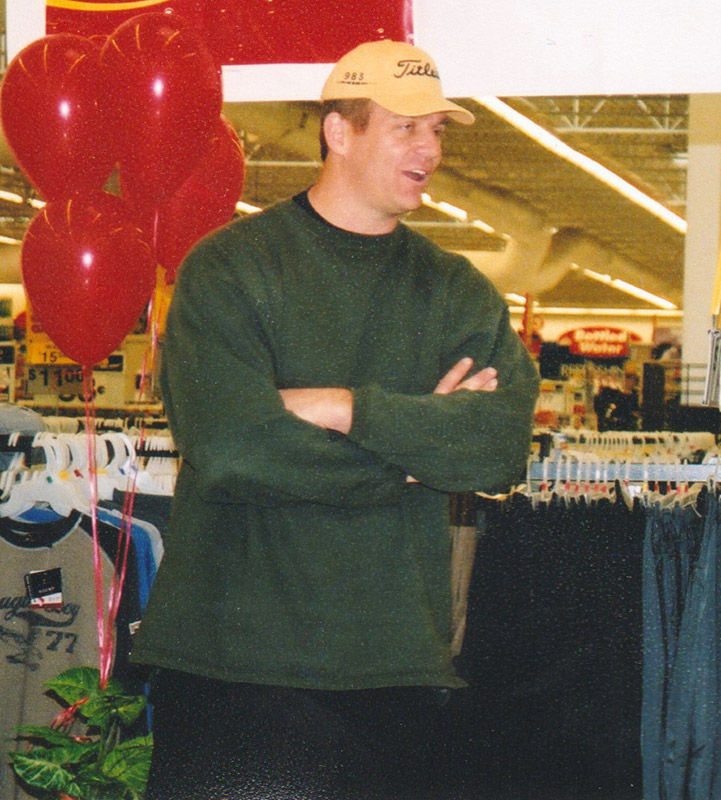 White man in sweater and cap standing next to balloons inside store