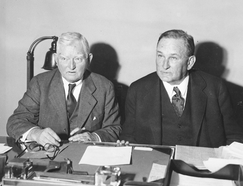 Two white men in suits seated at table