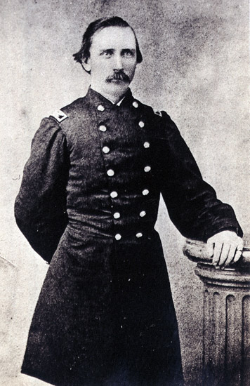 dark-haired white man with mustache in military uniform poses with left hand resting on a column