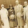 African-American man in suit holding hat standing on train platform with African-American man in suit and two women