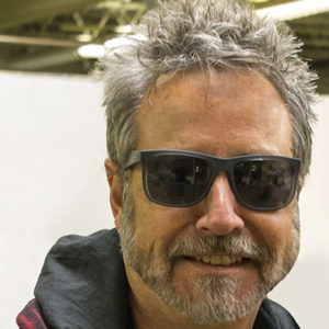 White man with beard and sunglasses smiling in hooded jacket