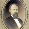 portrait photo in oval frame of White man with beard in black suit