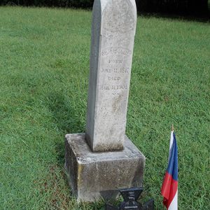Gravestone with cross marker in front of it and flag in cemetery
