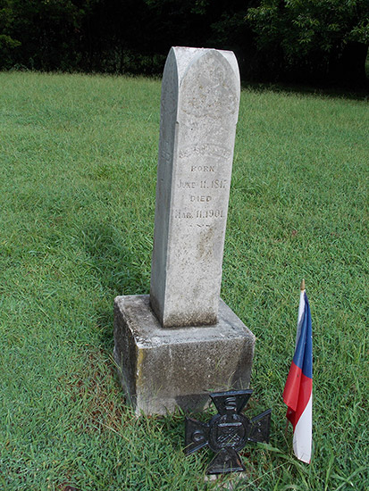 Gravestone with cross marker in front of it and flag in cemetery