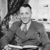 White man in suit sitting and smiling with open book in his lap